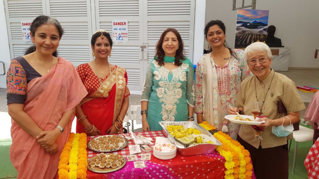 five woman standing while surrounding red table packed with Indian food
