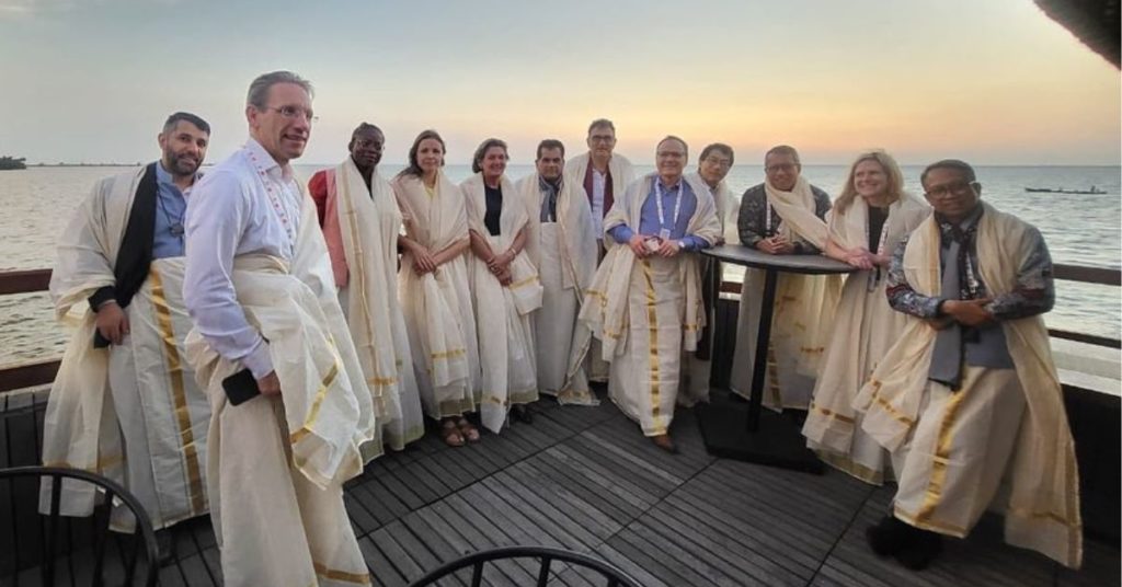 twelve people in India traditional white cloth standing at the edge of a deck. 
