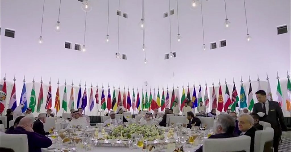 people sitting around a big round table in a room full of countries flag
